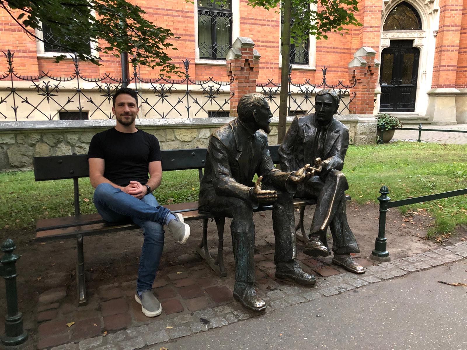 Yonatan seated beside the Mathematician's Bench sculpture in Krakow